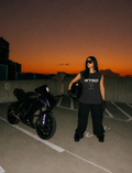 Person holding a helmet next to a motorcycle on a rooftop at sunset wearing a sleeveless tee streetwear acid washed
